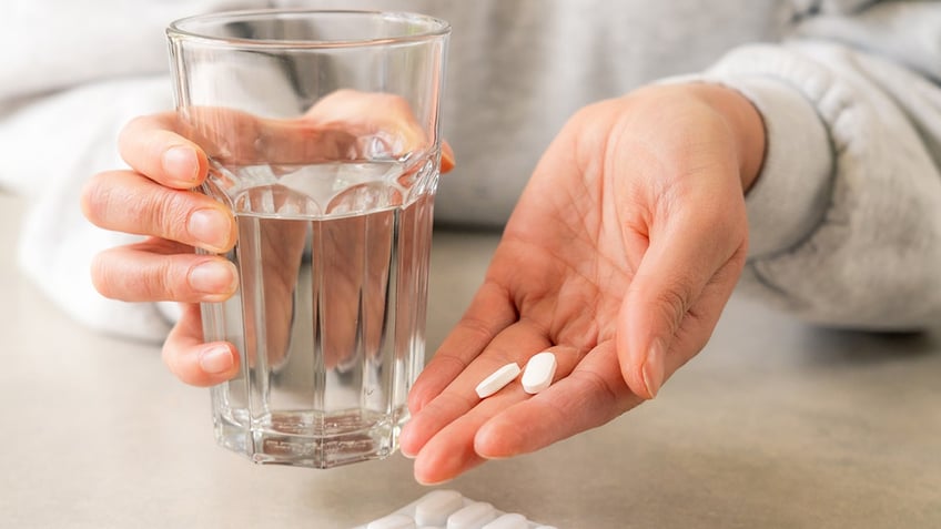 woman's hand ready to take medicine with a glass of water