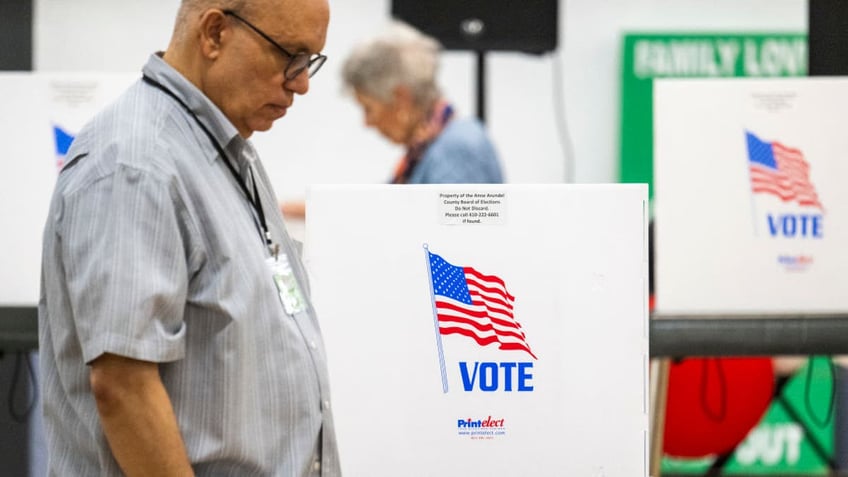 Maryland Board of Elections poll workers pass by empty booths during the Maryland state primary election