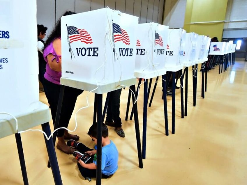 A woman votes from a booth as her child plays with a cellphone below inside the gymnasium