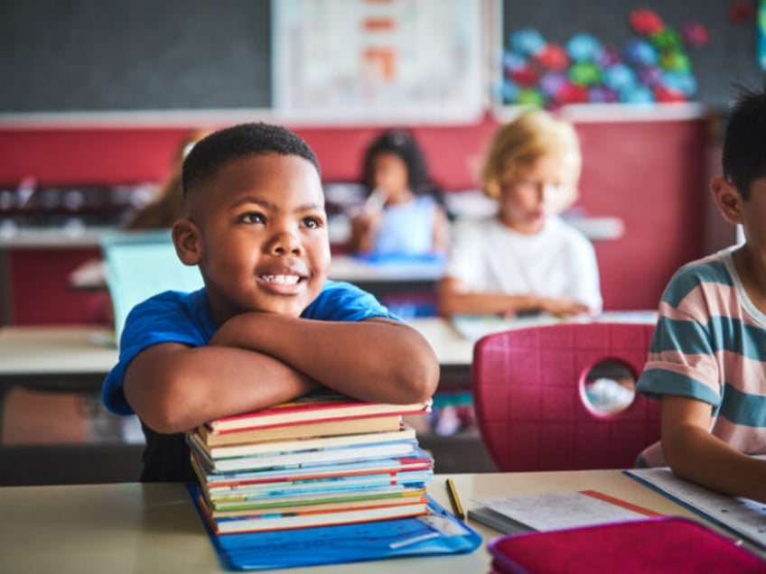 A young boy is smiling as he leans on books at his desk in class (Getty/Stock Photo).