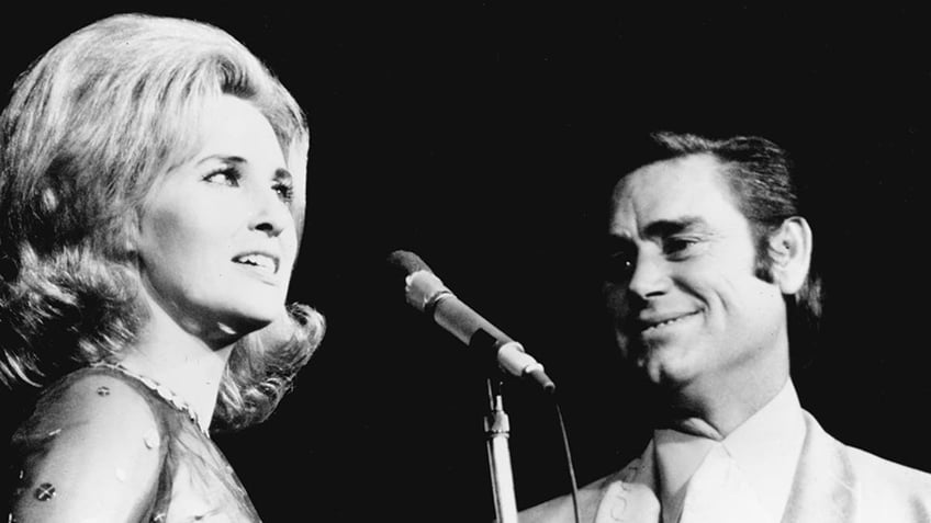 George Jones smiling looking at Tammy Wynette singing.