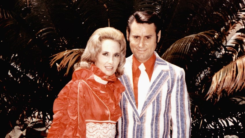 Tammy Wynette wearing a bright high color dress next to George Jones in a striped suit.