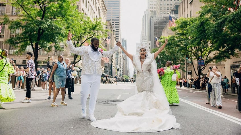 Bride and groom celebrating in the street holding their hands over their heads.