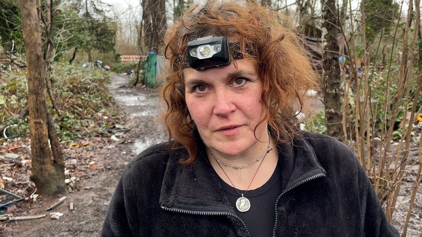 Woman with curly red hair wearing a headlamp stands in woods