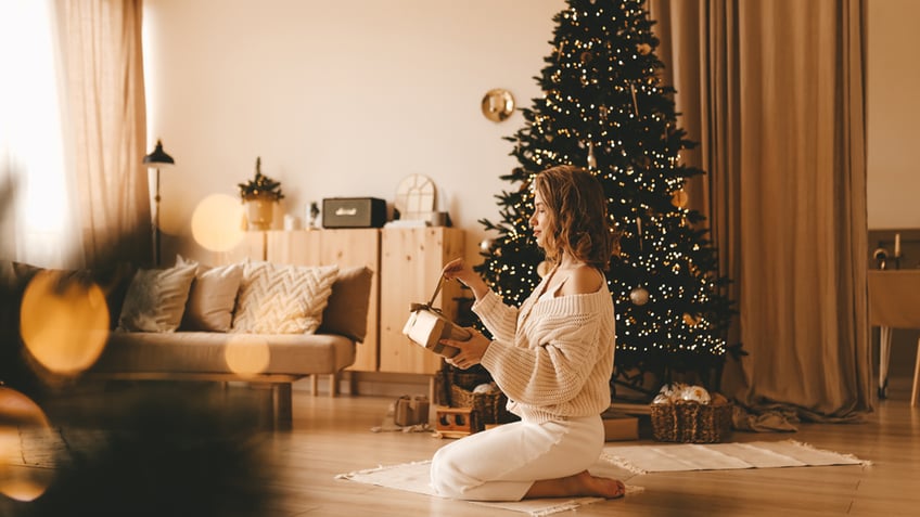 woman wrapping a present near her christmas tree