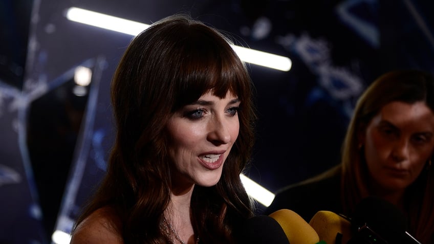 Dakota Johnson speaking into microphones on red carpet