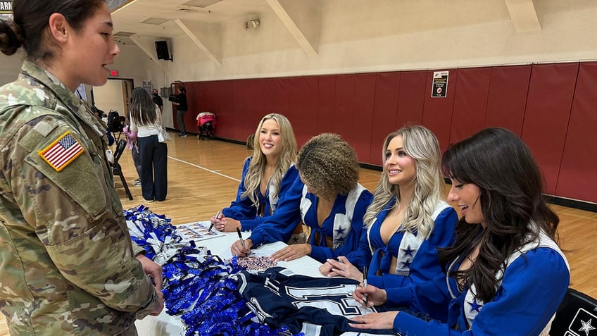 A servicewoman standing in front of several Dallas Cowboys Cheerleaders