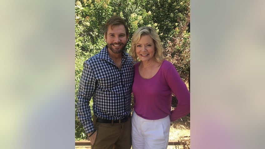 Sheree J. Wilson in a purple blouse and white pants posing next to William Keck in a plaid blue and white shirt and khacki pants.