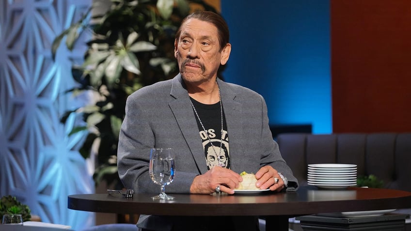 Danny Trejo looking serious while sitting at a table