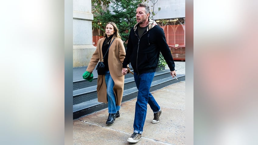 Kristen Bell in a camel colored long jacket walks hand-in-hand with husband Dax Shepard in a black jacket in New York