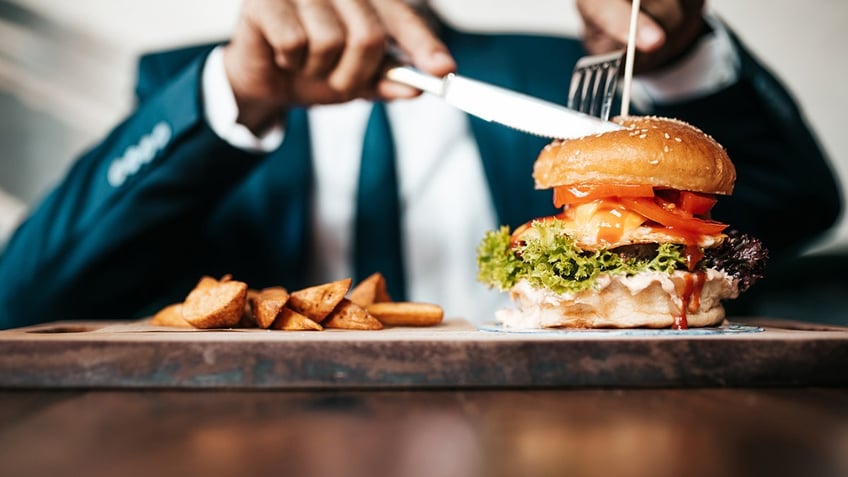 Handsome senior business man sitting in restaurant and enjoying in delicious burger. People and food concept.