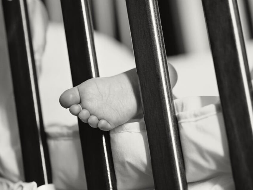 A child's foot sticking through the bars of a cot - stock photo