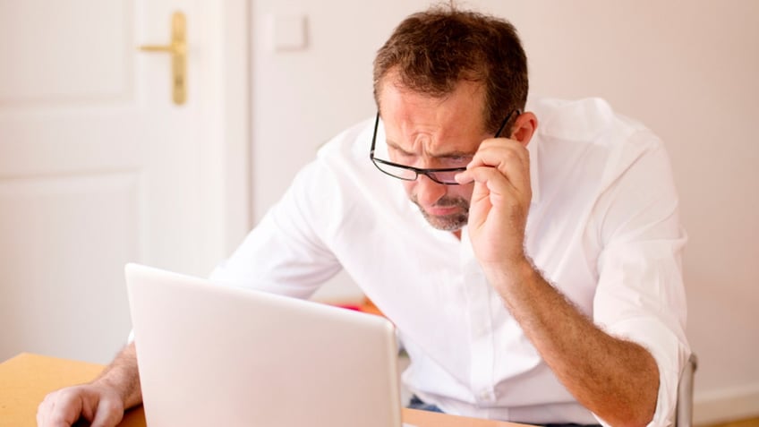 businessman sitting at desk and looking stressed at his laptop