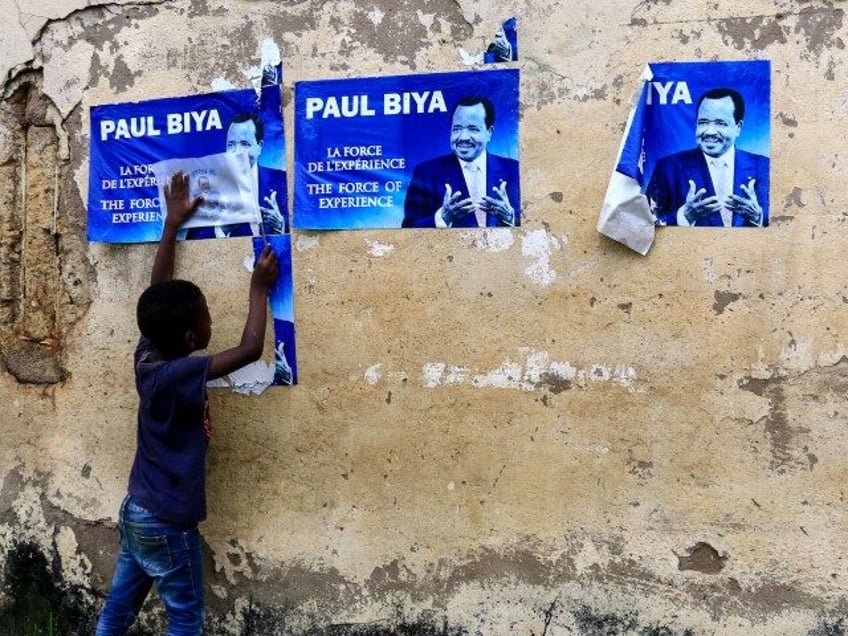 A young child holds posters of Cameroonian President Paul Biya on a wall in Yaoundé on No