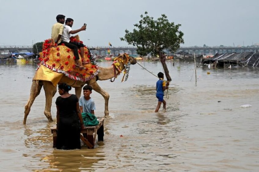 Men riding a camel across a flooded field on the banks of river Ganges in India on August