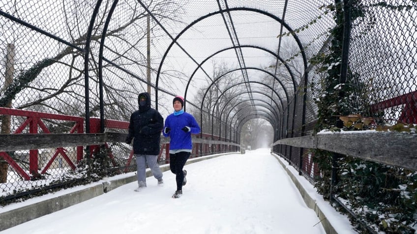 Runners run on a snow covered Monon Trial, Thursday, Feb. 3, 2022, in Indianapolis. A major winter storm with millions of Americans in its path is spreading rain, freezing rain and heavy snow further across the country. (AP Photo/Darron Cummings) 