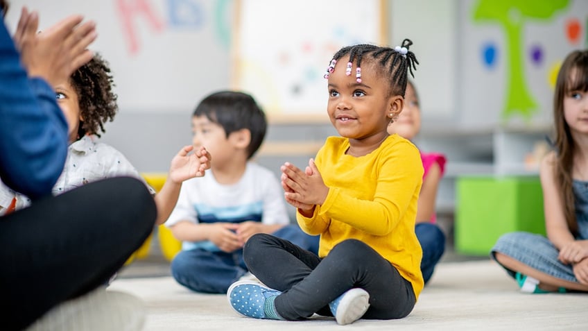 A small group of Kindergarten children sit on the floor of their classroom