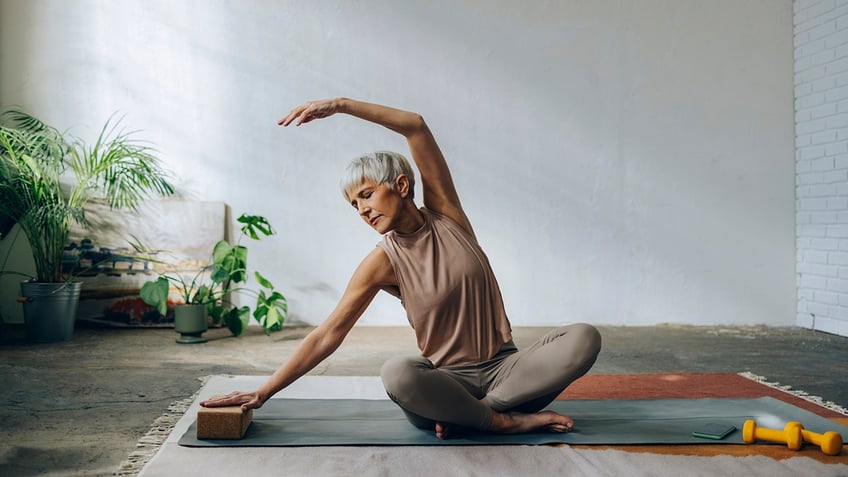 woman sitting on an exercise mat doing yoga and stretching