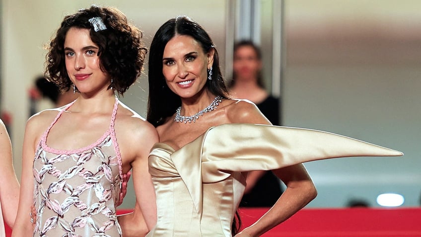 Demi Moore smiling alongside her co-star on the red carpet wearing a satin dress