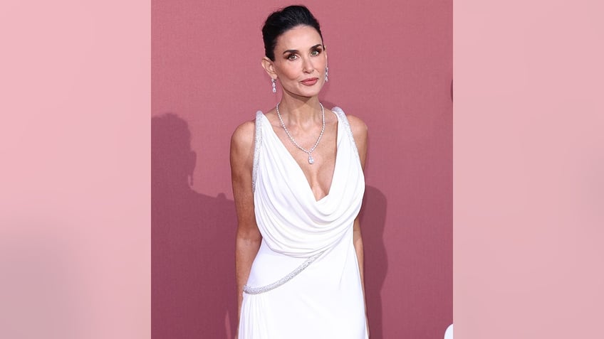 Demi Moore has her arms behind her as she poses in a drooping V-neck white dress on the carpet in France