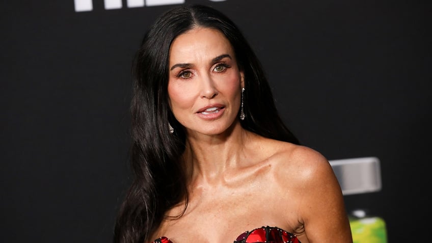 Demi Moore looks slightly to her left in a red and black strapless dress at "The Substance" Los Angeles premiere