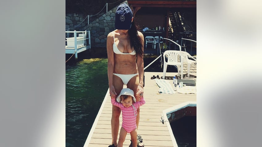 Demi Moore in a white bikini and hat holds granddaughter Louetta's hands while walking on a dock