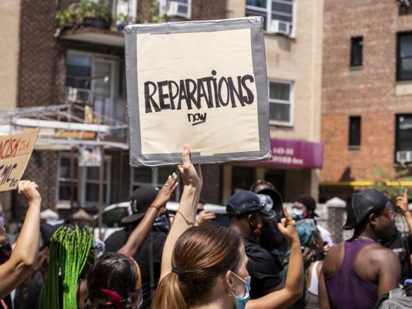 A large crowd of protesters wearing masks and carrying signs that say, "Reparations N