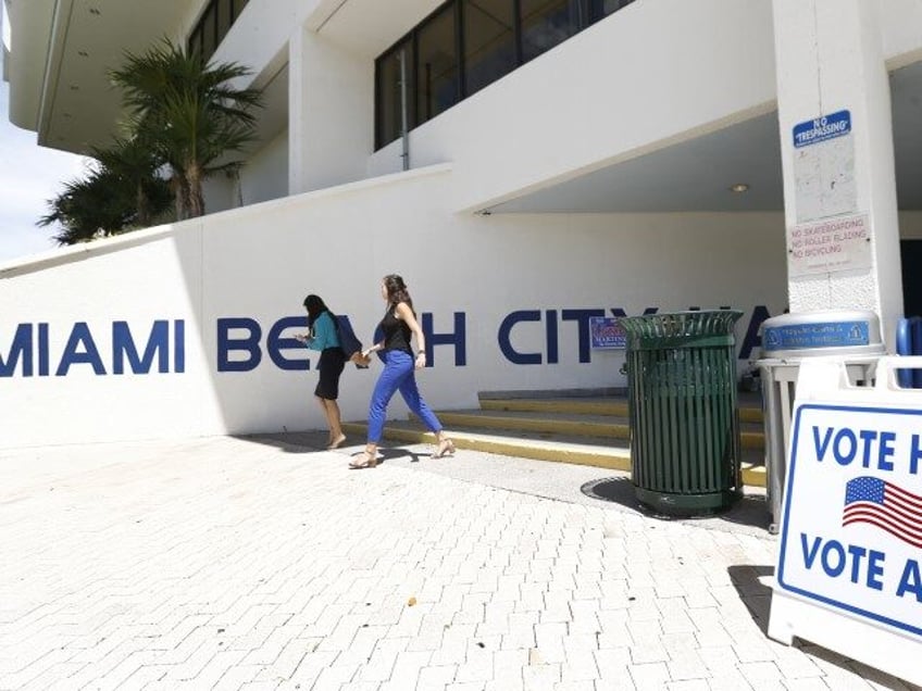 Pedestrians walk past a sign for a polling station at Miami Beach City Hall, Monday, Aug.