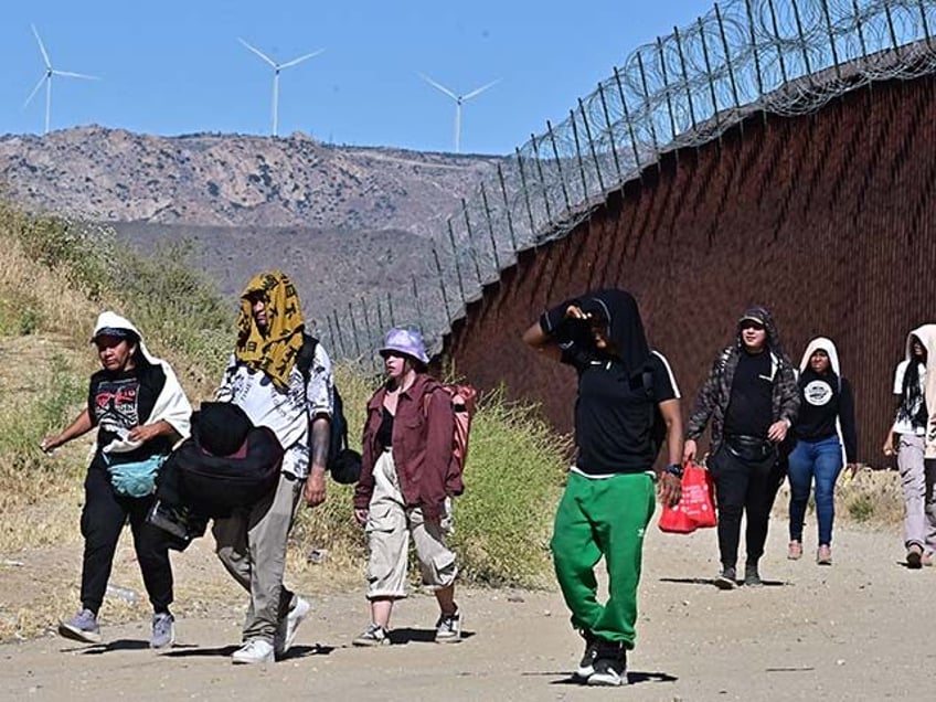 Migrants walk on the US side of the border wall in Jacumba Hot Springs, California on June