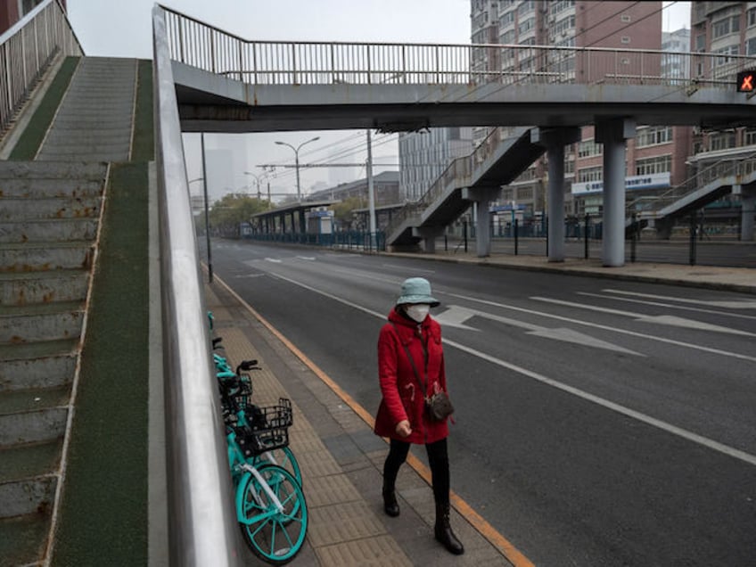 BEIJING, CHINA - NOVEMBER 24: A woman wears a mask to prevent the spread of COVID-19 as she walks alone next to a nearly empty street near the Central Business District on November 24, 2022 in Beijing, China. China recorded its highest number of COVID-19 cases since the pandemic began …