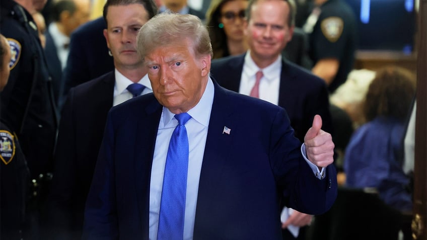 Donald Trump in blue tie, dark coat giving thumbs up