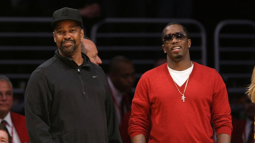 Sean Diddy Combs wears a red sweater with Denzel Washington at a basketball game.