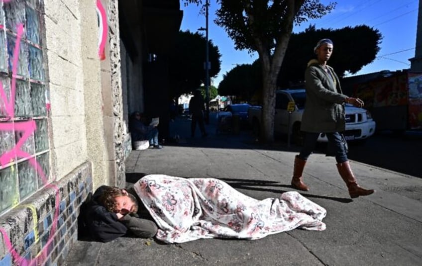 A homeless man sleeps on a sidewalk in Los Angeles, California on November 22, 2023 -- one of thousands to do so