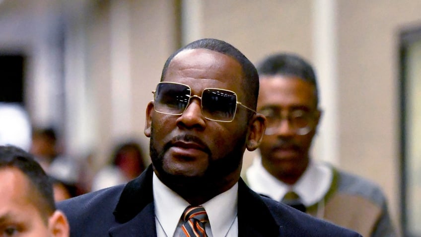 R Kelly wears a blue coat and red tie outside of court