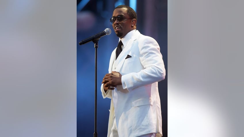 Diddy in a white suit performing in front of a mic.