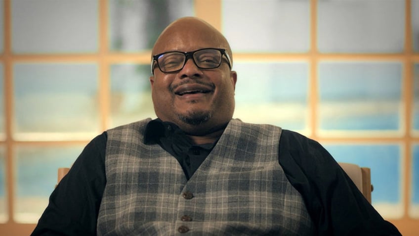 Todd Bridges wearing a vest and smiling with glasses.