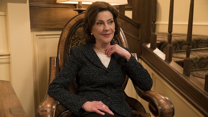 Kelly Bishop in character wearing a grey sweater and sitting on a chair.