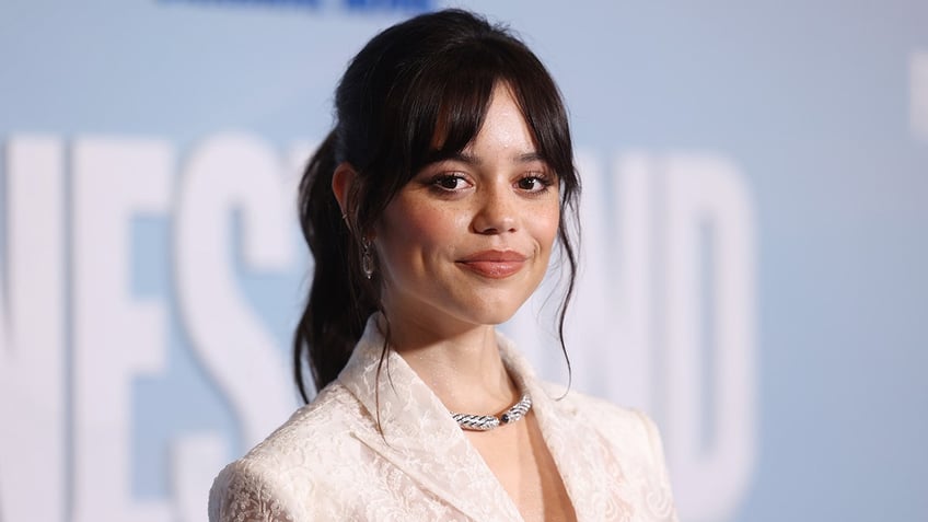 Jenna Ortega soft smiles in a white blazer on the carpet