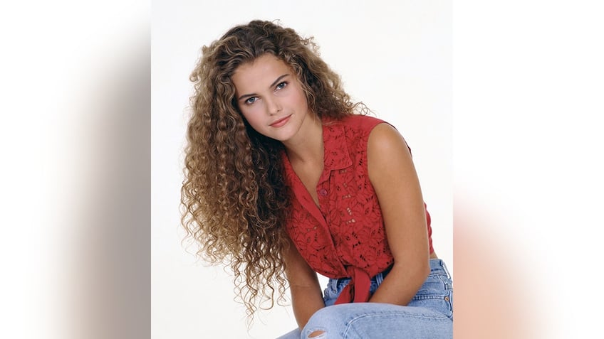 Kerri Russell with extremely curly hair in a red top and jeans soft smiling in a portrait