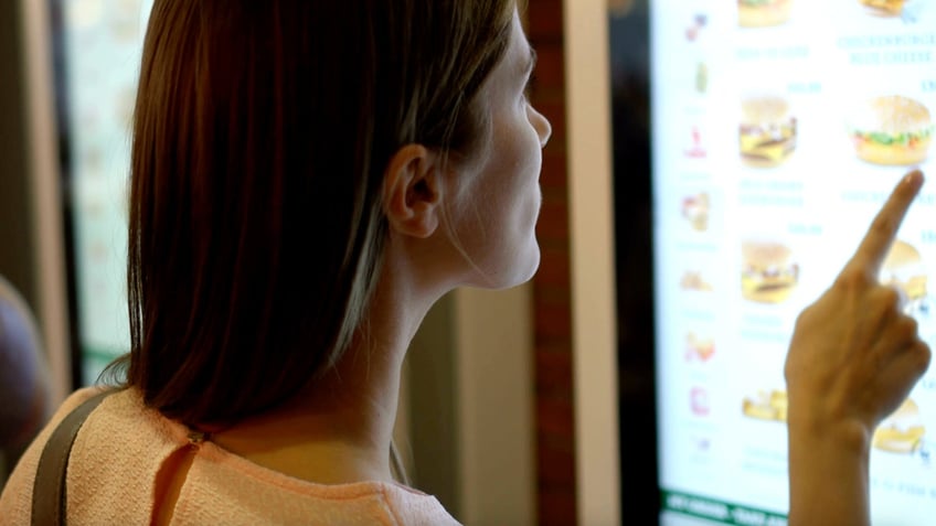 A woman orders fast food from a digital self-serve screen.