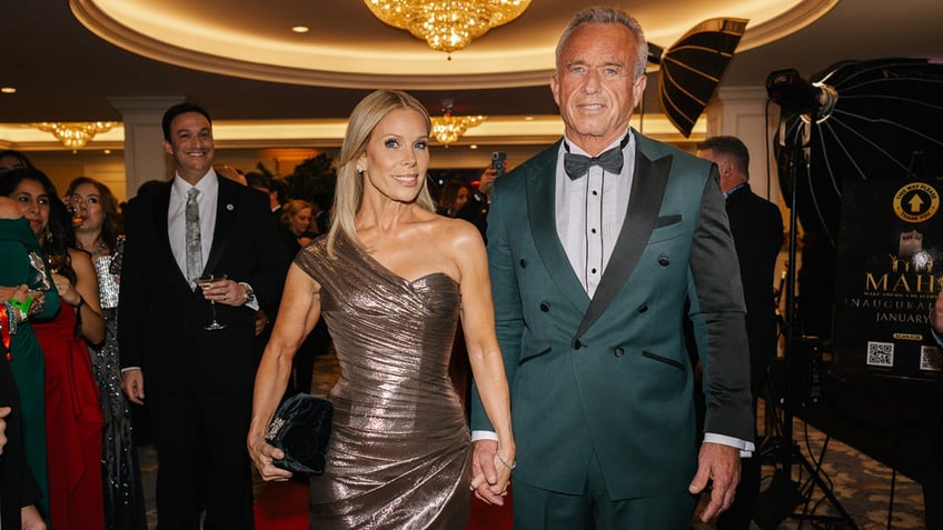 Cheryl Hines shines in gold dress next to Robert F. Kennedy Jr. in green suit.