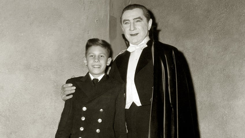 Bela Lugosi dressed as Dracula with his arm wrapped around his son on set.