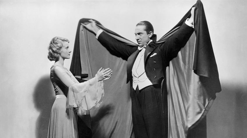 Bela Lugosi opening up his cape to an actress.