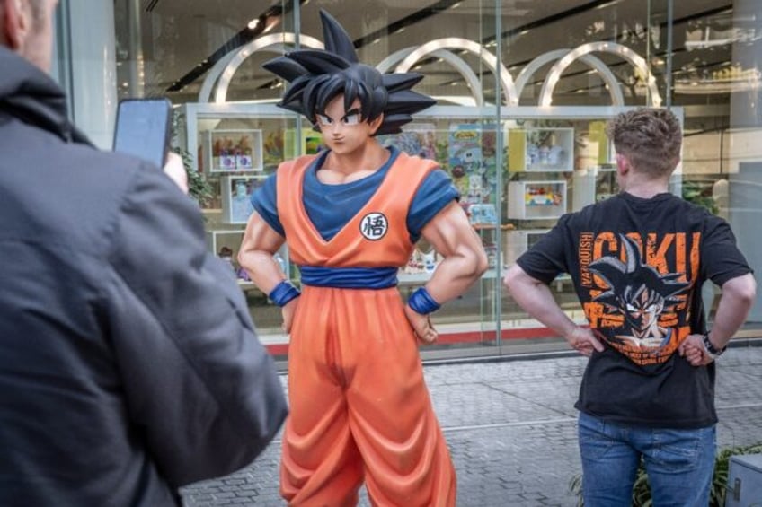 A tourist wearing a T-shirt of Dragon Ball has his photographs taken with a statue of Drag