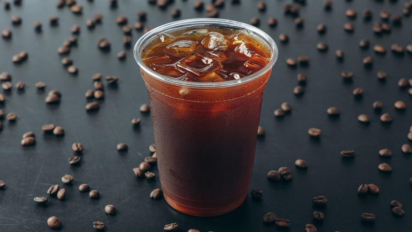 A cold brew is shown on a black background littered with coffee beans.