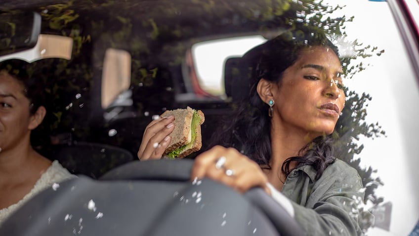 woman drives while eating a sandwich