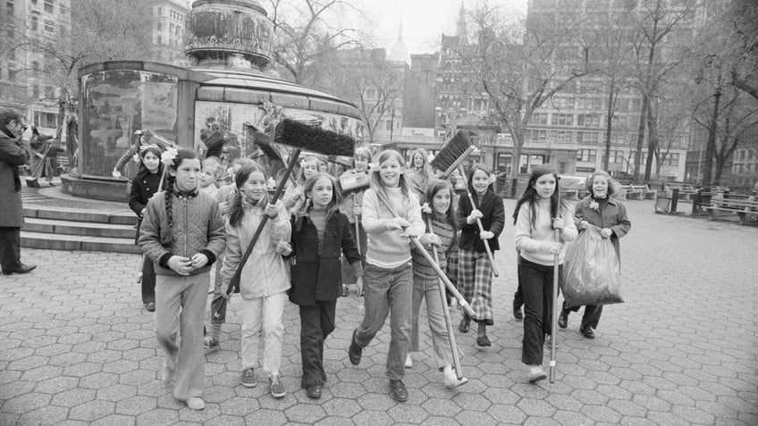 A group of girls carries brooms through a park on the first Earth Day in New York City as they head for the area they were assigned to clean up.