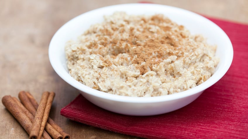 A bowl of oatmeal rests next to some cinnamon sticks.