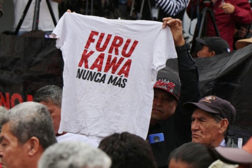 A man in Ecuador holds up a shirt with the slogan 'Furukawa, never again,' alluding to a J