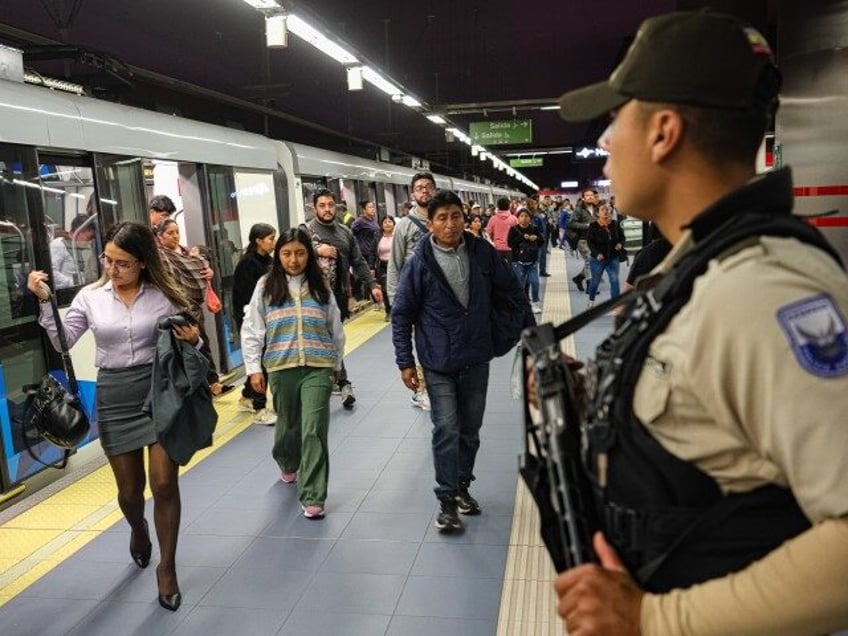 Police officers stand guard as commuters walk by at a subway station on January 10, 2024, in Quito, Ecuador. President Noboa declared "internal armed conflict" after hooded and armed men broke into TC Television's live broadcast, among other violent incidents across the country on Tuesday. Ecuador has been hit by …